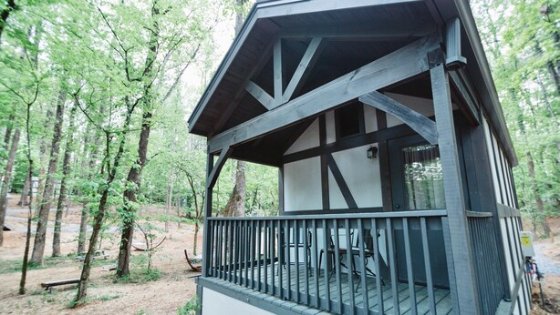 A wooden cabin with a balcony, surrounded by trees. - #10 Helena - Tiny Home Cottage (Sevierville)