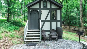 A small wooden cabin with a door and steps, two Adirondack chairs, and a bench outside. - #10 Helena - Tiny Home Cottage (Sevierville)