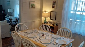 A dining area with a wooden table set for four, surrounded by white chairs with wooden seats. - Port Clyde Village House   -   Summer of 2026 is booked. See you in 2027 (St George)