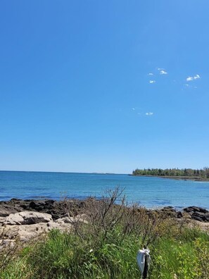 A coastal landscape with a rocky shoreline, clear blue sky, and distant land.