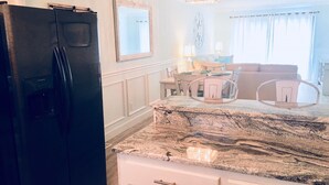 Una cocina con refrigerador negro, armarios blancos y encimera de mármol.