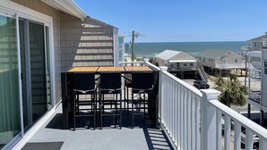 Balcón con mesa y sillas, con vista a una playa y otros edificios.