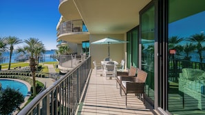 Un balcón con vista a la piscina, muebles de exterior y barandilla de vidrio.