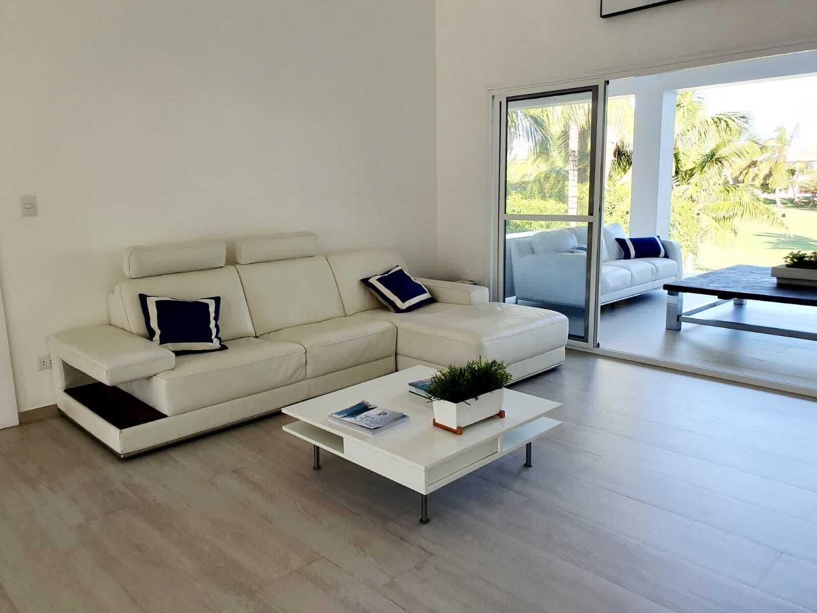 Una sala de estar moderna con un sofá blanco, una mesa de centro y vistas a través de un ventanal.