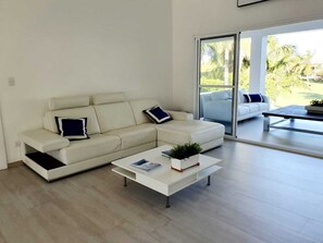 A modern living room with a white sofa, a coffee table, and a view through a glass door. - Luxury, 1 of a kind, Lake-view Villa on Golf course (Punta Cana)