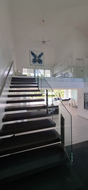 A modern interior with a staircase leading to a second floor, a ceiling fan, and a large window.