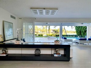 A modern living room with a large window, a black console table with decorative items, and a view of a pool and greenery outside.