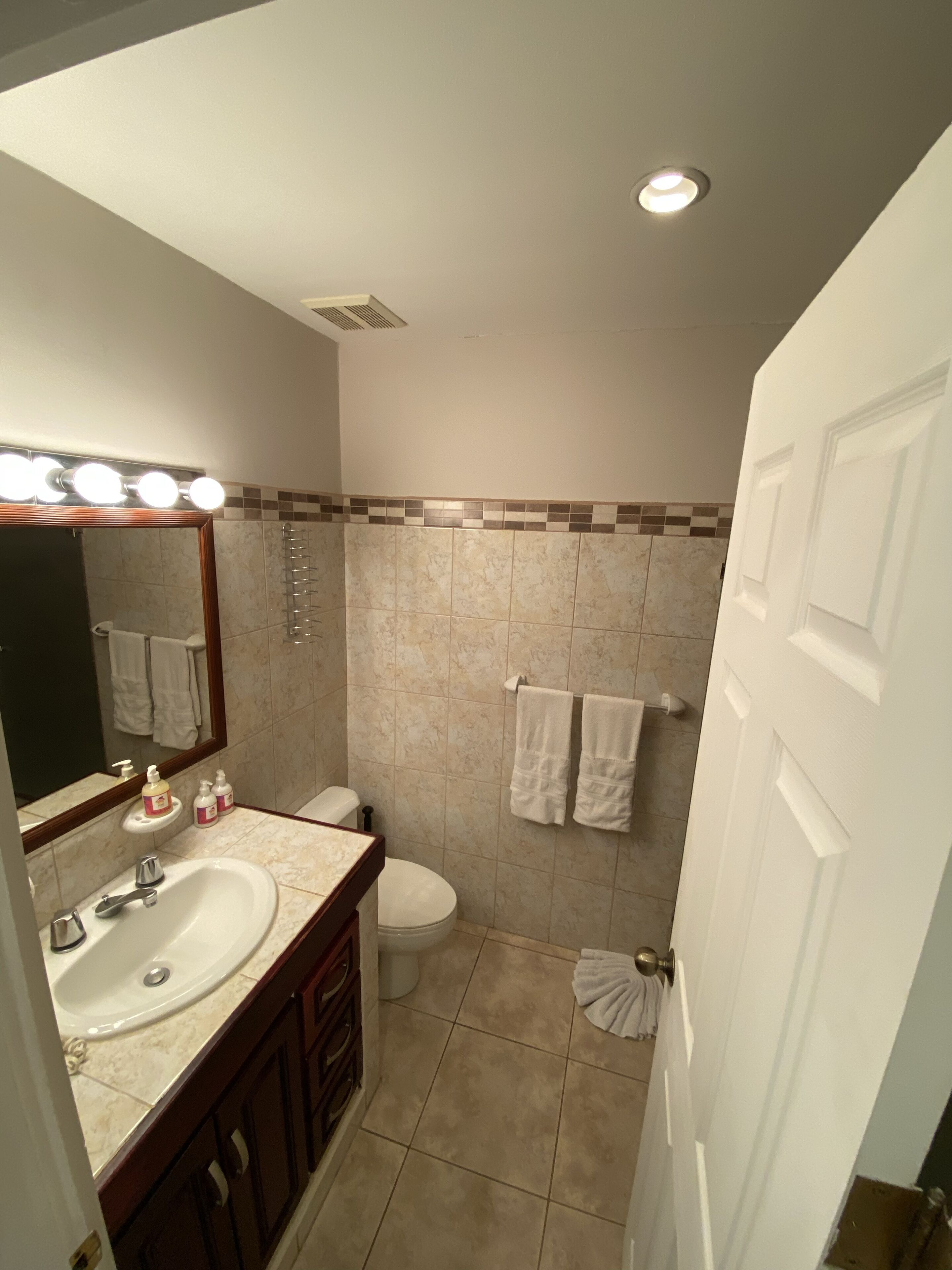 Un baño con tocador, lavamanos, espejo con iluminación, inodoro y zona de ducha.