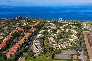 Vista aérea de um resort à beira-mar, com vários edifícios, quadra de tênis e uma praia.