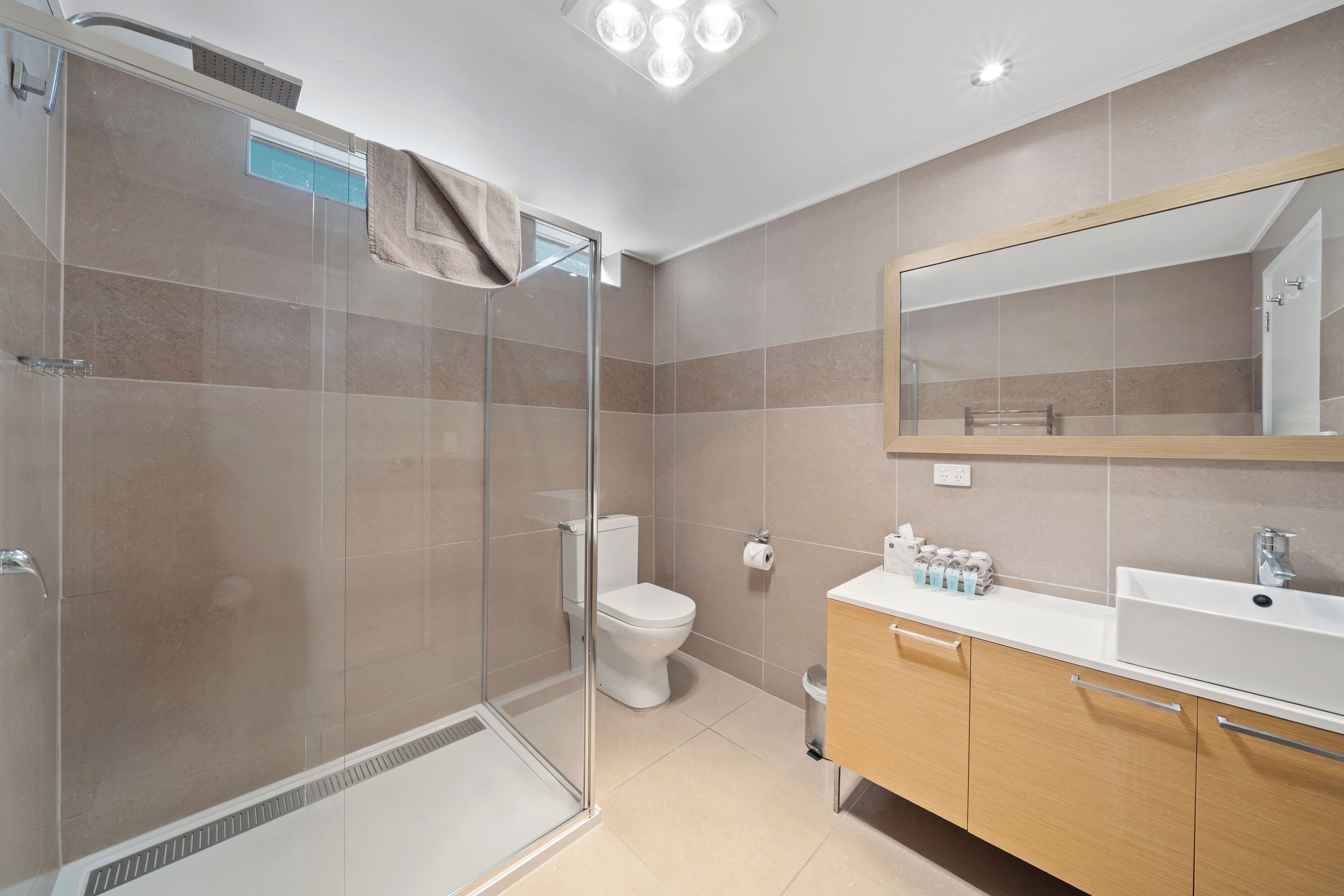 Een moderne badkamer met een glazen douchecabine, een toilet, een wastafel met spiegel en een afvalbak.