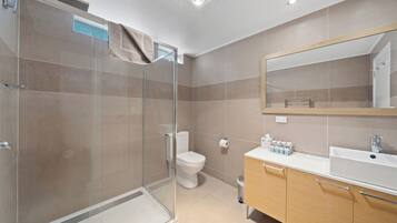 Een moderne badkamer met een glazen douchecabine, een toilet, een wastafel met spiegel en een afvalbak.