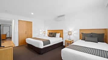 Habitación de hotel con dos camas, un armario de madera, un escritorio y una mesita de noche con lámparas.