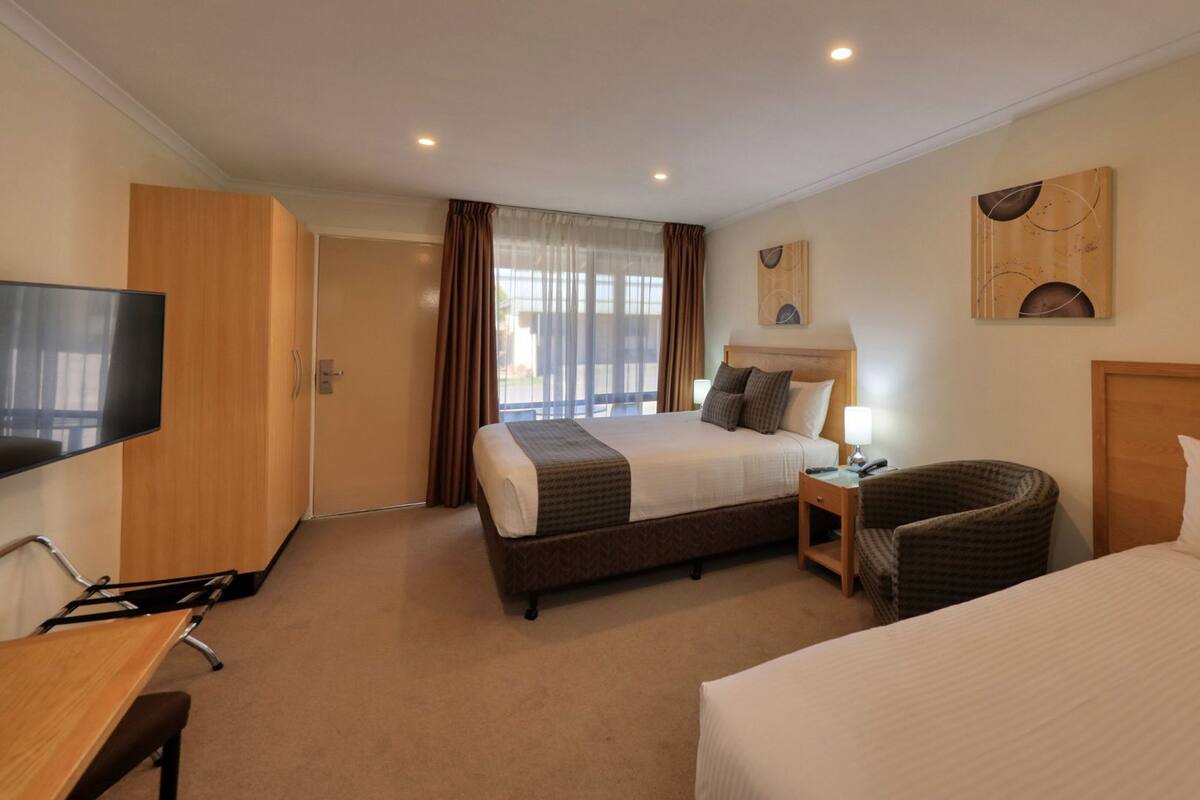 Ein Hotelzimmer mit zwei Betten, einem Fernseher, einem Schreibtisch und einem Sessel.