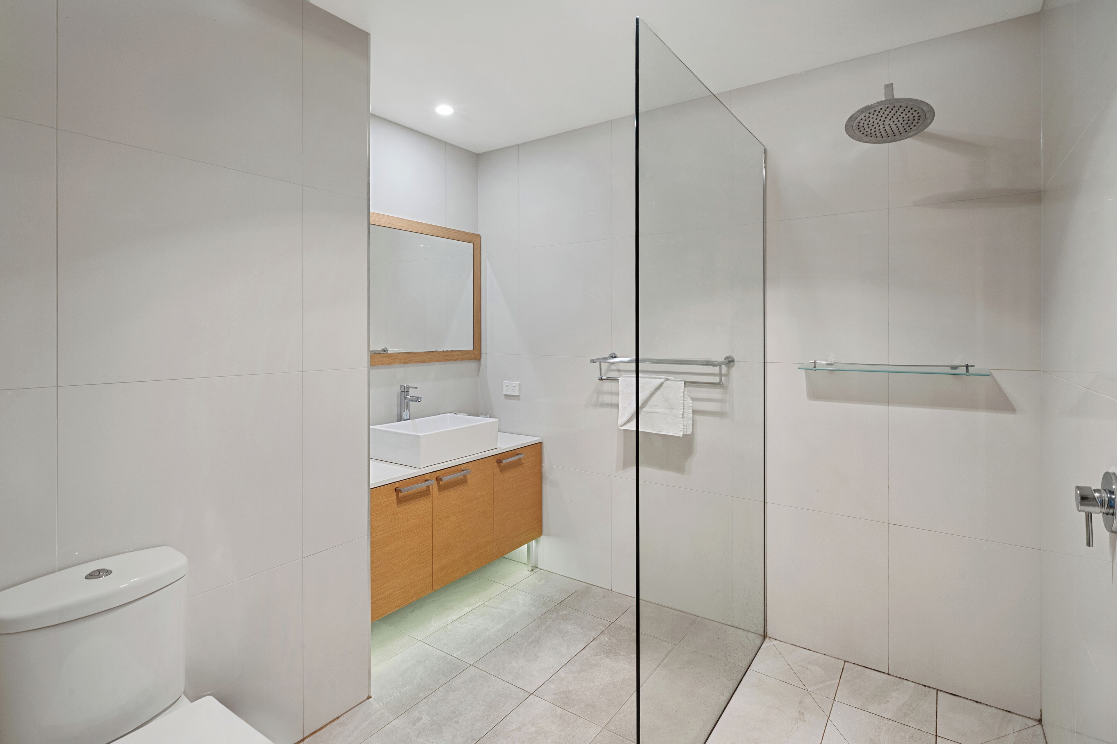 A modern bathroom with a glass shower enclosure, a wooden vanity, and a white toilet.