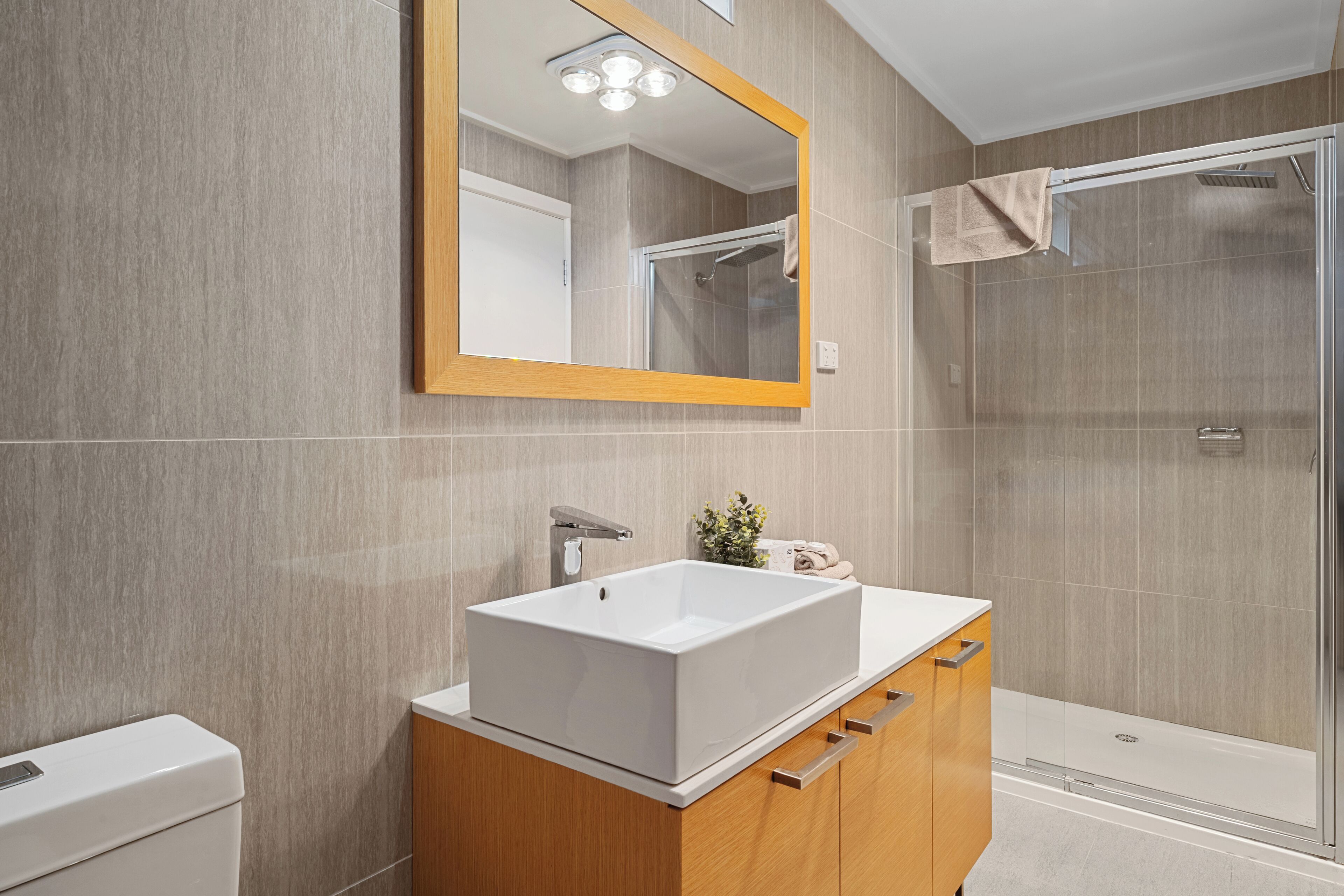 Un baño moderno con un lavamanos grande y rectangular, muebles de madera, un espejo y una cabina de ducha de vidrio.