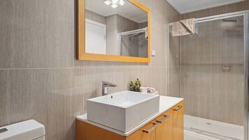 Un baño moderno con un lavamanos grande y rectangular, muebles de madera, un espejo y una cabina de ducha de vidrio.