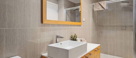 Un baño moderno con un lavamanos grande y rectangular, muebles de madera, un espejo y una cabina de ducha de vidrio.