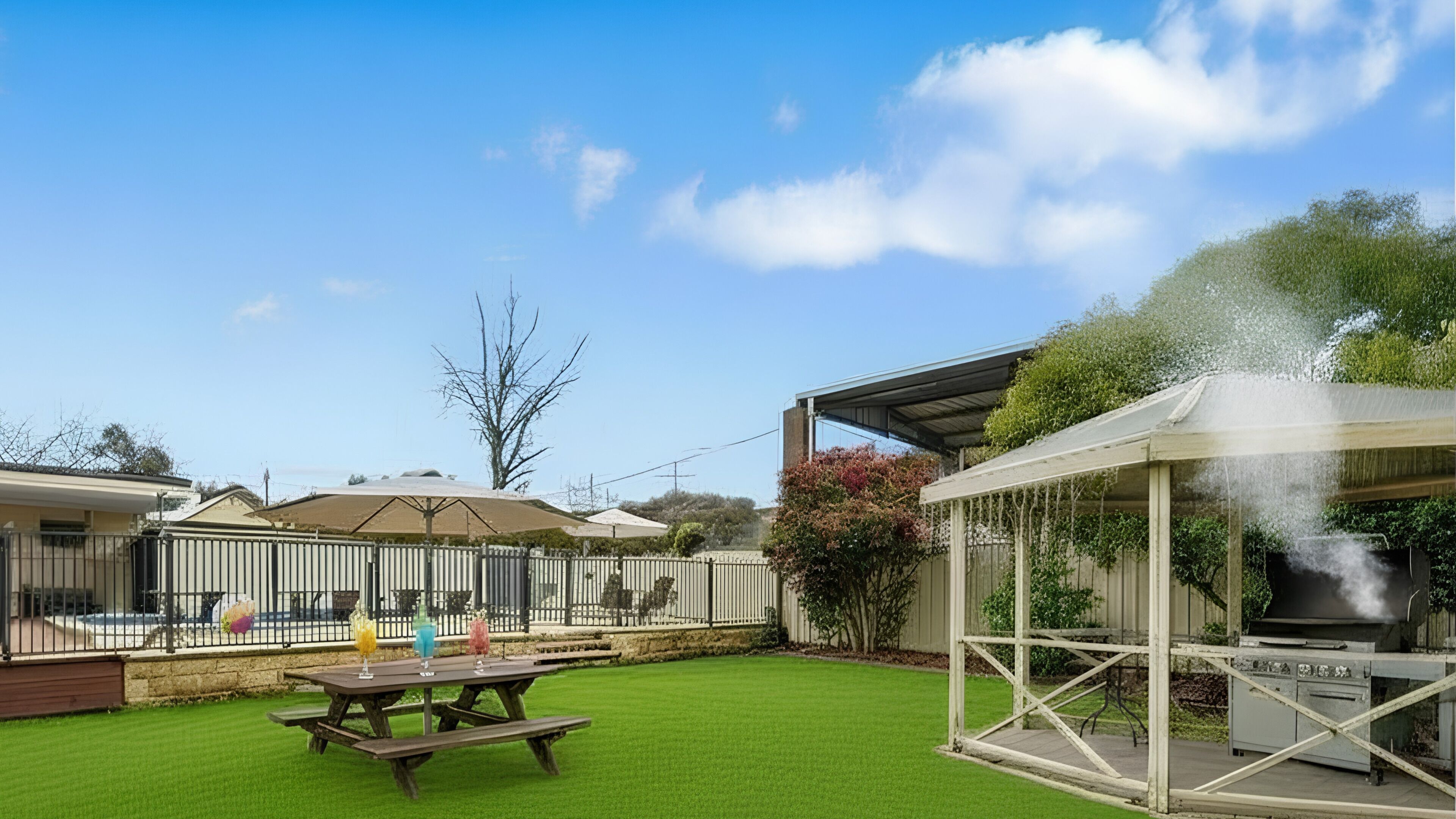 A backyard with a barbecue grill, a picnic table, and a covered area with a chimney emitting smoke.
