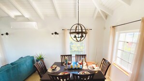 A dining area with a wooden table, chairs, a chandelier, and a view of the outdoors through a window. - Waterfront Villa, Private Pool & Kayaks (Cooper Jack Bay Settlement)