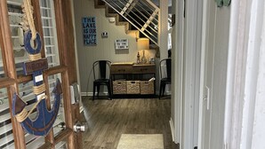 Un couloir avec une porte en bois, une pancarte de bienvenue, un banc et une vue sur un escalier.