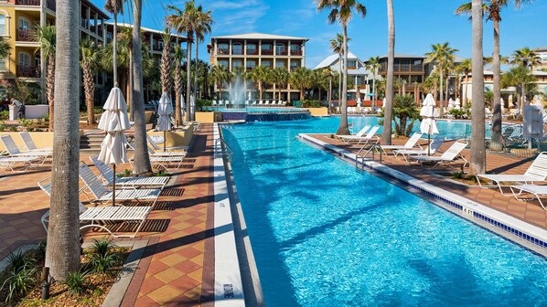 Piscina con sillas de descanso y palmeras, rodeada de edificios de hotel.