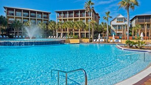 Una gran piscina al aire libre con una fuente, rodeada de palmeras y sillas de descanso.