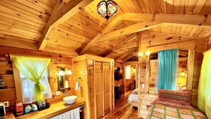 A wooden cabin interior with a wooden bed, a wooden dresser with a sink, and a mirror. - #15 Queenie - Gypsy Cottage (Sevierville)