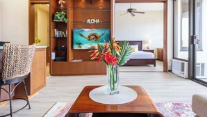 Een moderne hotelkamer met een houten entertainmentkast, een groot flatscreen televisietoestel, een bed, een plafondventilator en een groot raam.