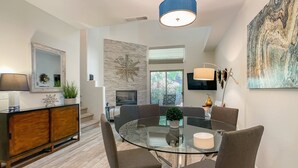 A modern dining area with a glass table, comfortable chairs, a wooden cabinet, and a large abstract painting.