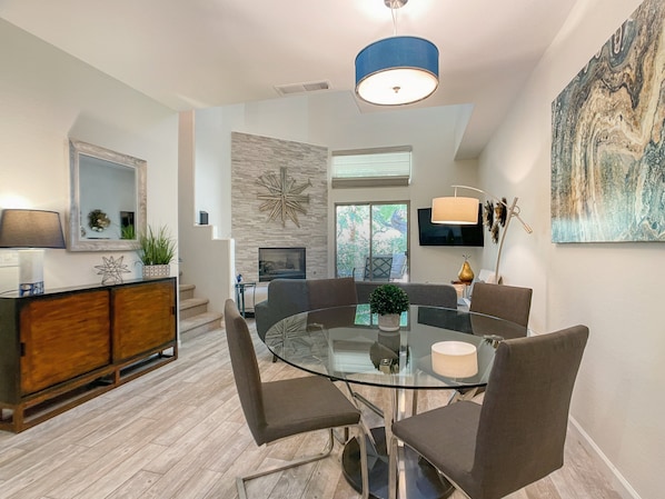 A modern dining area with a glass table, comfortable chairs, a wooden cabinet, and a large abstract painting.