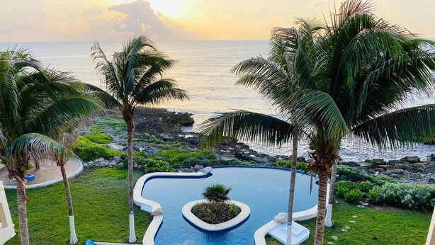 A pool area with lounge chairs and palm trees, overlooking a rocky coastline. - Oceanfront Penthouse -4300 Sq Ft, 2 Level -Mi Casa Del Mar (Akumal)