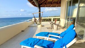 A terrace with white lounge chairs and blue cushions, a hanging hammock, and a view of the ocean. - Oceanfront Penthouse -4300 Sq Ft, 2 Level -Mi Casa Del Mar (Akumal)