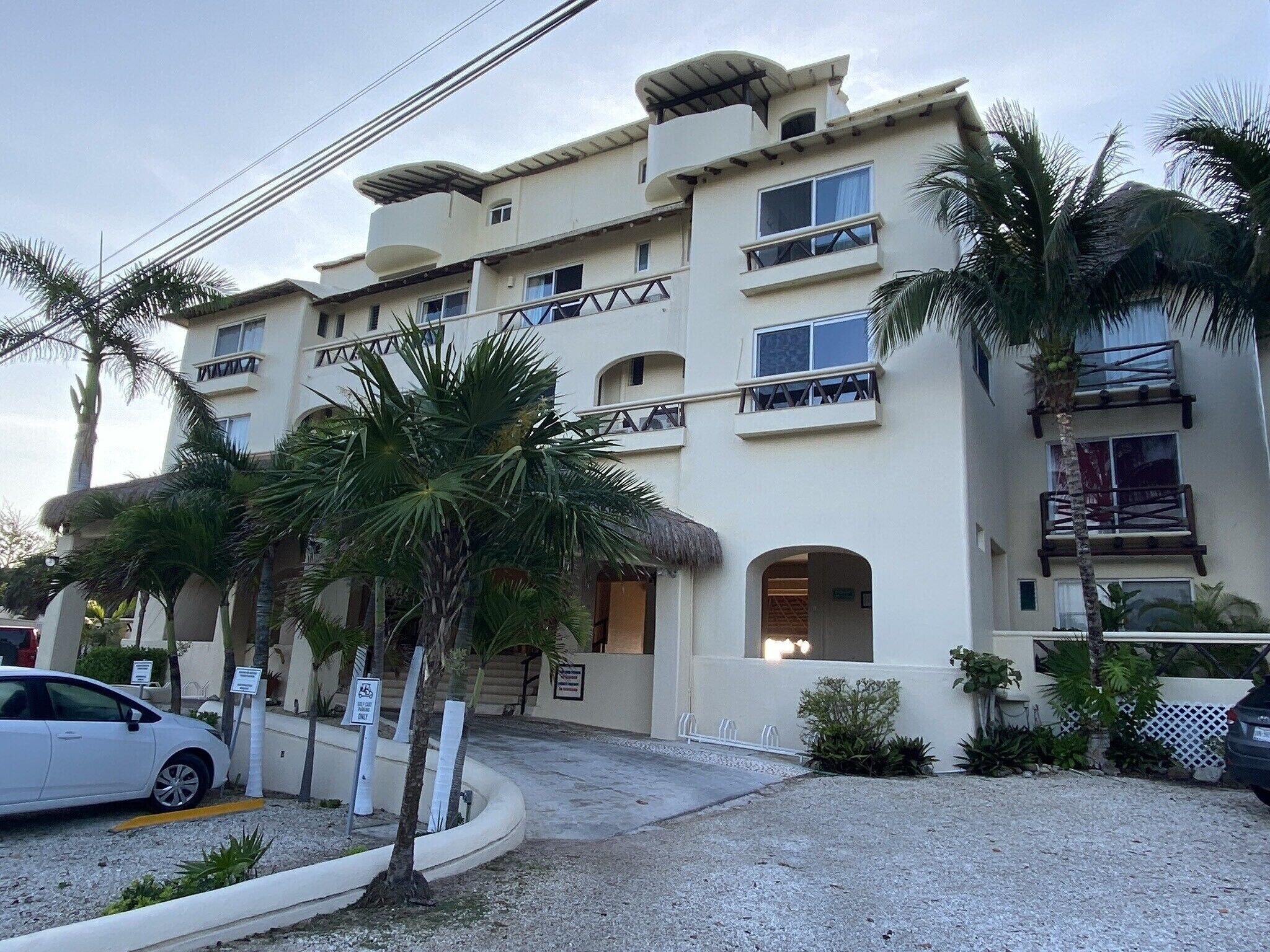 A multi-story hotel with balconies, palm trees, and a parking area.