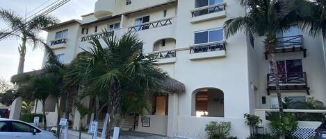 A multi-story hotel with balconies, palm trees, and a parking area.