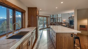 A modern kitchen with a large island, wooden cabinetry, and a view of the mountains. - Tahoe Point of View by Tahoe Getaways - Hot Tub + Sauna + Lake Views + Private Beach (Tahoe City)