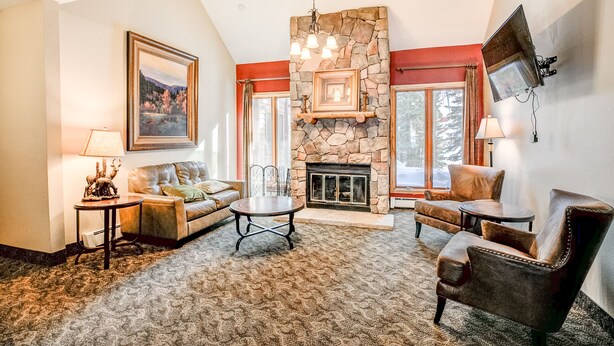 A cozy living room with a stone fireplace, a sofa, a coffee table, and a TV mounted on the wall.