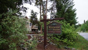 A sign for Wildwood Suites with 1 & 2 bedroom condos, surrounded by trees and a stone pathway.