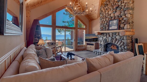 A cozy living room with a stone fireplace, a large window overlooking a scenic view, and a plush sofa.