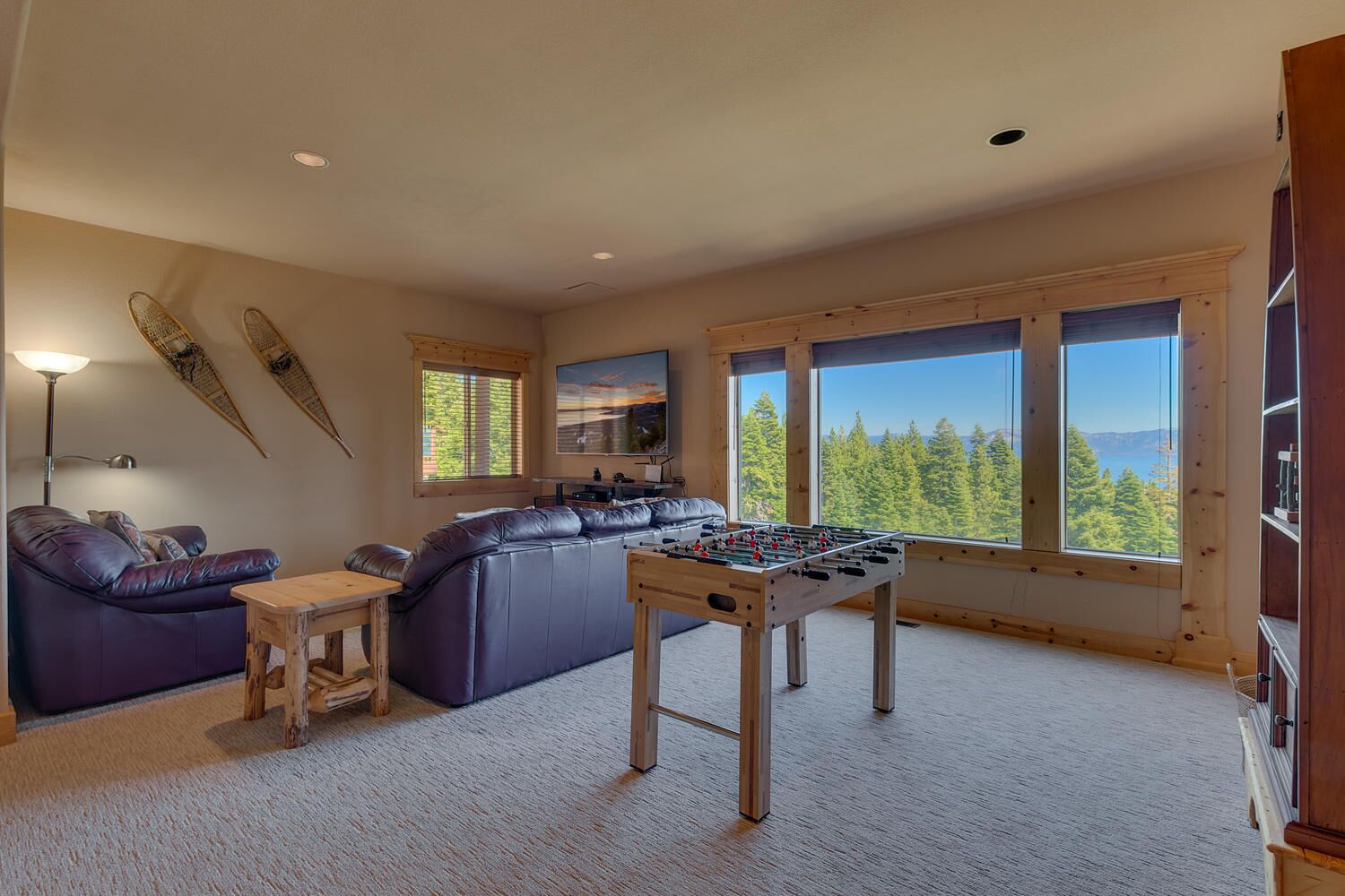 Una sala de estar acogedora con un sofá grande, una mesa de fútbol y vistas a un bosque a través de amplios ventanales.