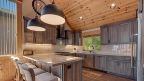 A modern kitchen with wooden cabinets, a central island with bar stools, and pendant lighting.