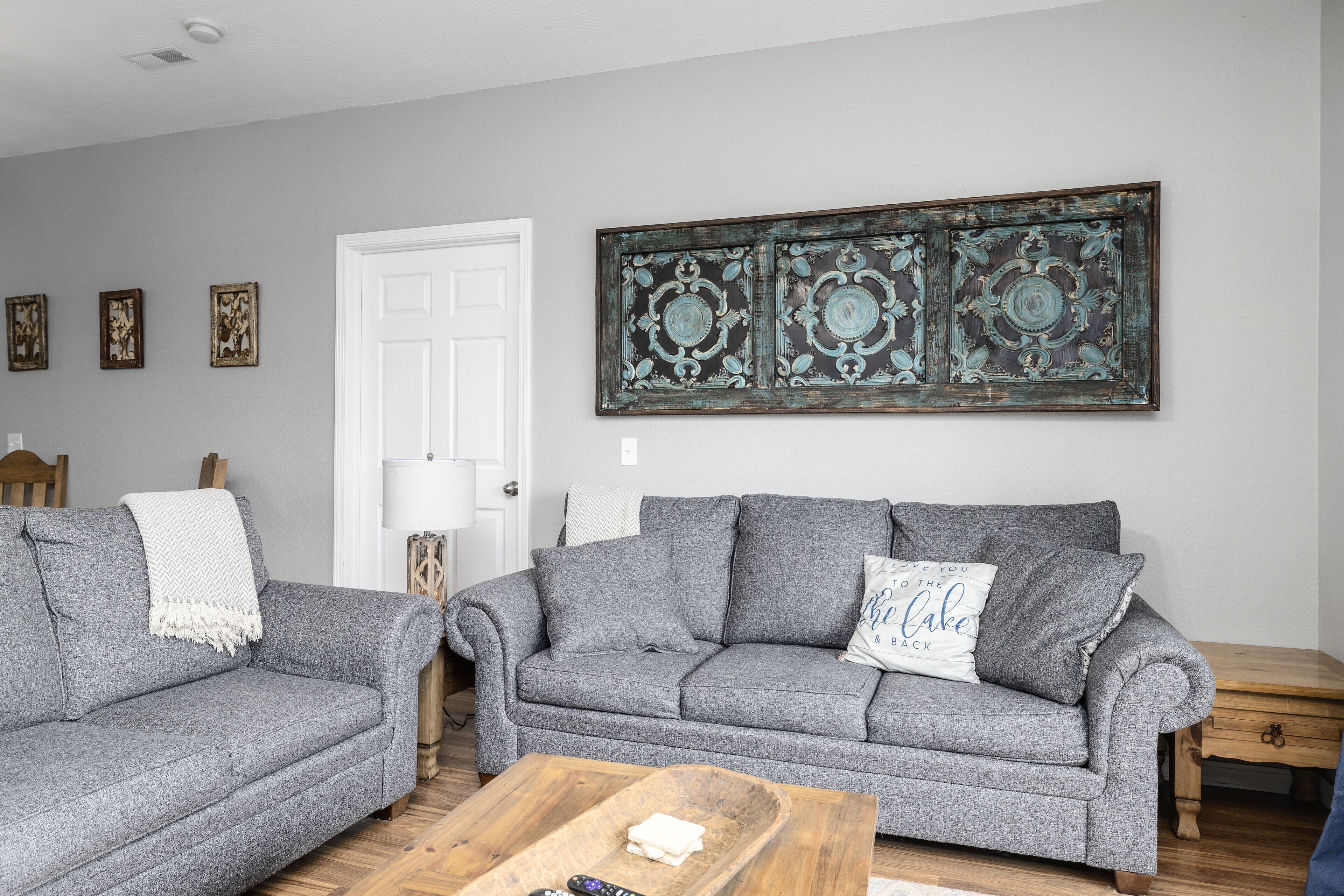 A living room with two grey sofas, a wooden coffee table, and a decorative metal artwork on the wall.