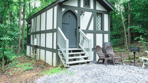 Une petite cabane à un seul étage, avec une porte grise et des boiseries blanches, entourée d’arbres.