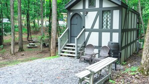 Une petite cabane avec une véranda, un banc et deux fauteuils Adirondack.