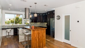 Une cuisine moderne dotée d’un îlot central en bois, d’appareils électroménagers en acier inoxydable et d’une grande fenêtre offrant une vue sur la verdure.