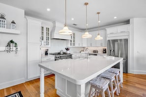 A modern kitchen with white cabinetry, a large island, pendant lighting, and stainless steel appliances.