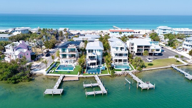 Uma área residencial costeira com várias casas de dois andares, uma piscina e um cais que se estende para a água.