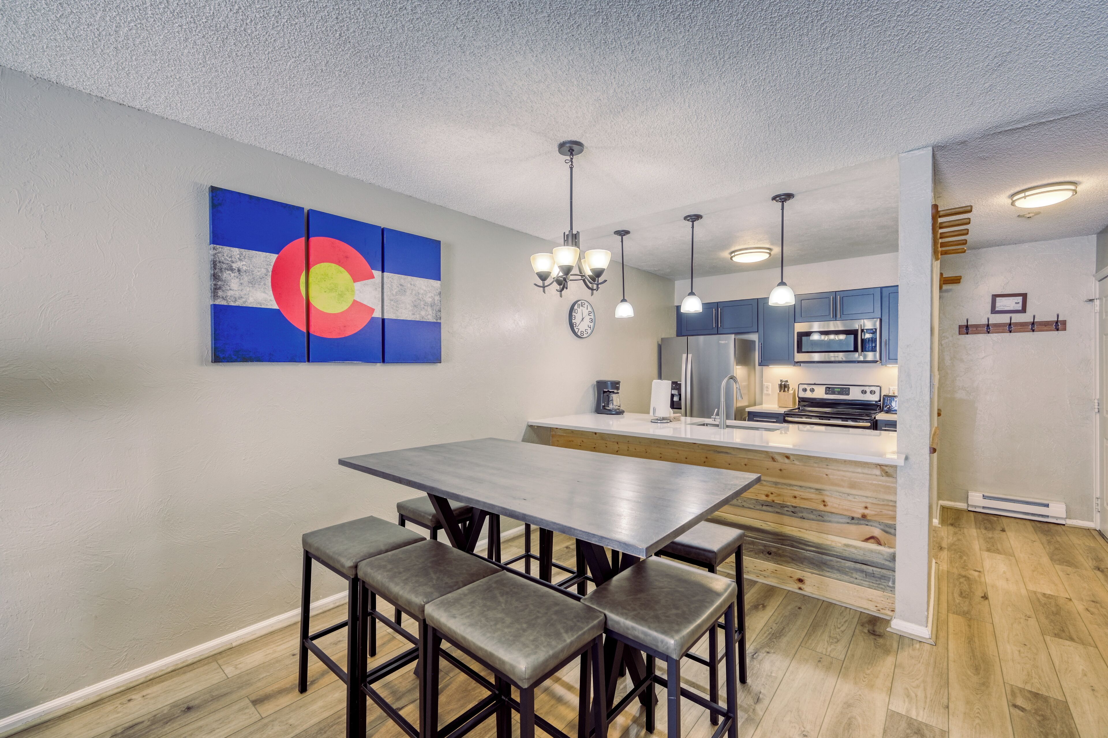 A modern kitchen with a central island, a dining area with a table and benches, and a large wall art piece.