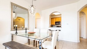 A dining area with a glass table, white chairs, a bench, a chandelier, and a kitchen visible through an archway. - Top Floor*Balcony*VistaCay Convention Ctr & iDrive (Orlando)