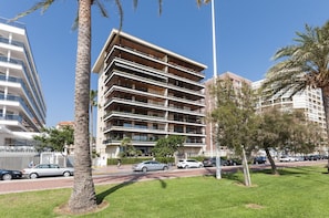 Residents enjoy balconies with outdoor space in this urban building surrounded by lush greenery and palm trees.