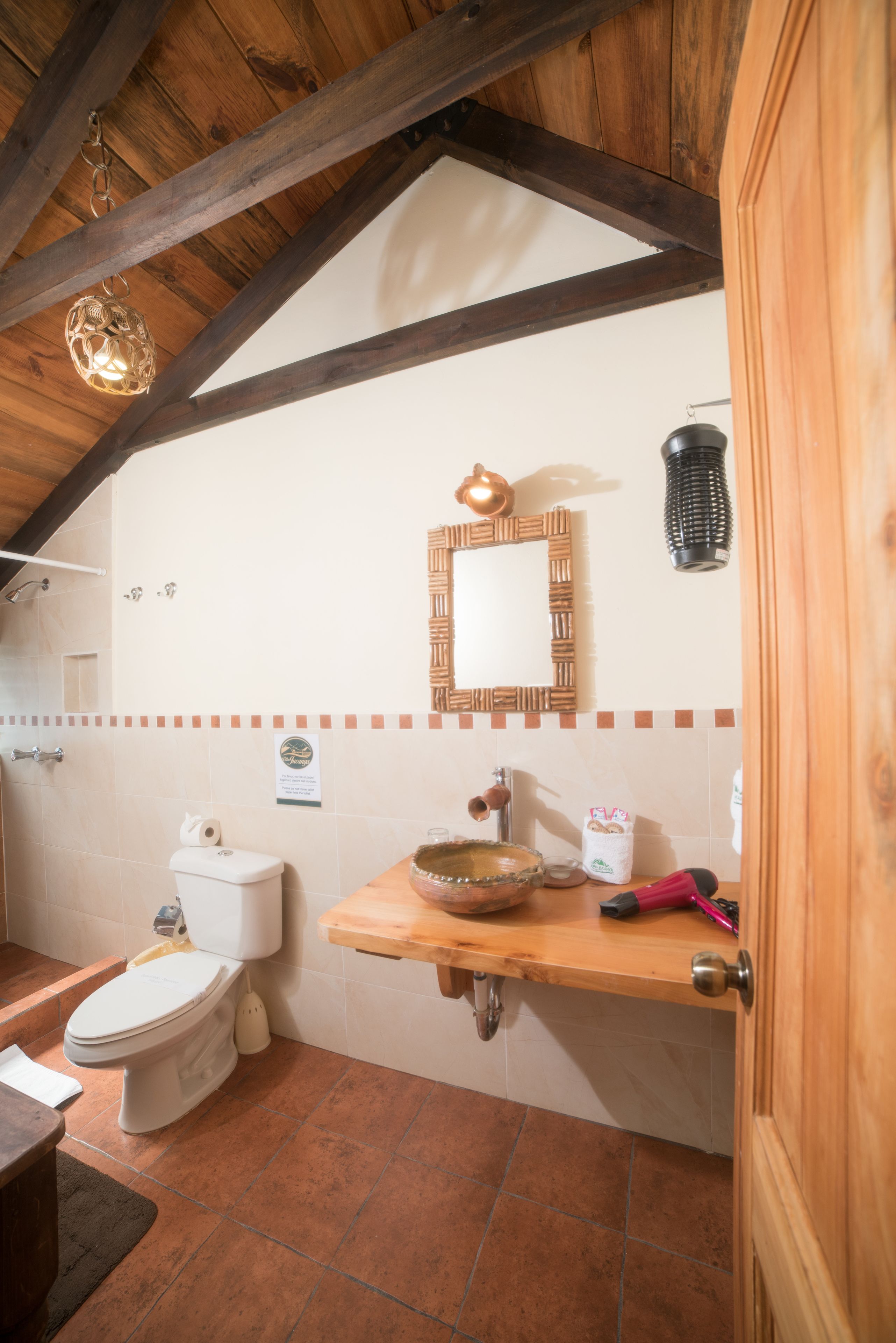 A rustic bathroom with a wooden ceiling, a wooden shelf with toiletries, a mirror, and a toilet.